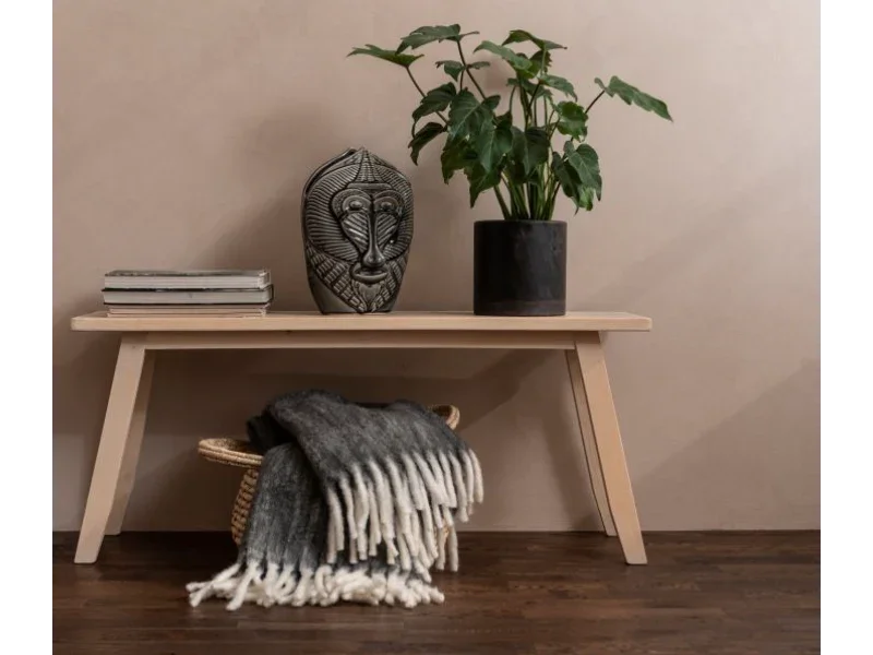 Minimalistisk træbænk med plaid i kurv, grøn plante og dekorativ maske, stueinteriør