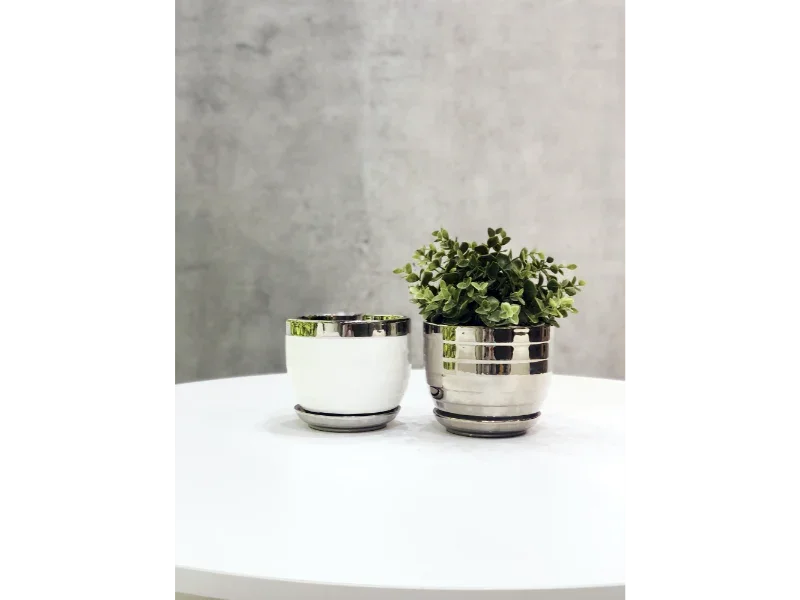 To moderne keramik krukker med metalfinish, én med grøn plante, på hvidt bord.